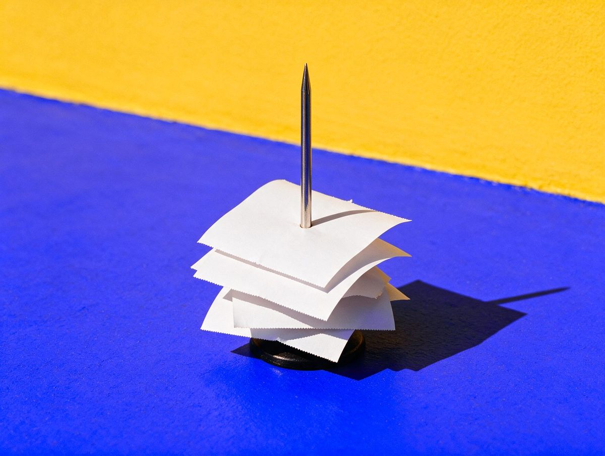 A steel bar spike stacked with blank order tickets, on a cobalt floor against a saffron wall: at 7CEAS, every order goes from the table to the bar to the till.
