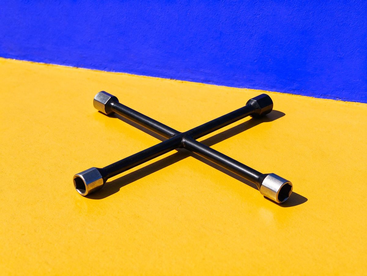 A four-way wheel brace on a saffron floor against a cobalt wall: at Mario's Tyre Service, one tool fits every size, and one booking form works in six languages.