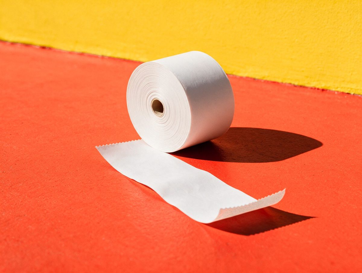 A roll of till paper beside a torn blank receipt, on a vermilion floor against a saffron wall: Counter, the till built around your floor.