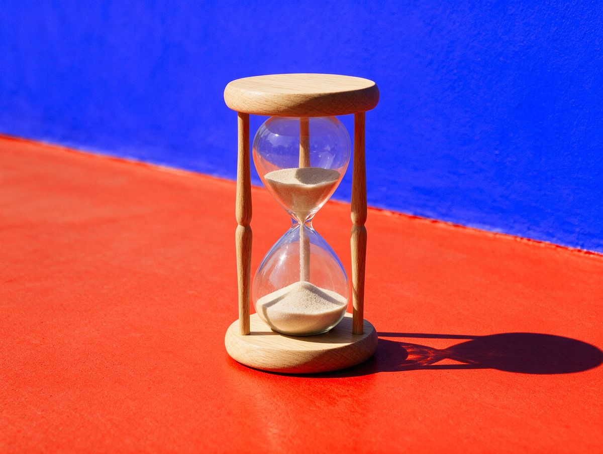 An oak hourglass on a vermilion floor against a cobalt wall: it works in both directions, like our sites in English and Arabic, and keeps time across time zones.